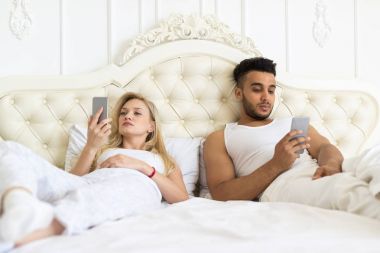 Genç çift yatak, ciddi üzgün Hispanik erkek ve kadın akıllı cep telefonu kullanarak ayrı yalan