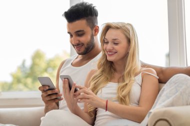 Genç güzel çift pencere, yakınındaki Koç kullanarak hücre akıllı telefon mutlu gülümseme İspanyol kadın erkek oturmak