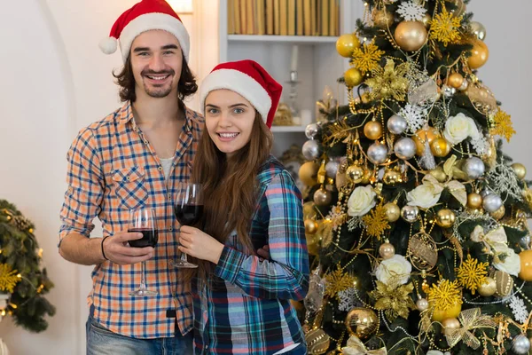 Christmas Holiday Happy Couple Hold Wine Glasses Stand Near Decorated New Year Tree Wear New Year Santa Hat — Stock Photo, Image