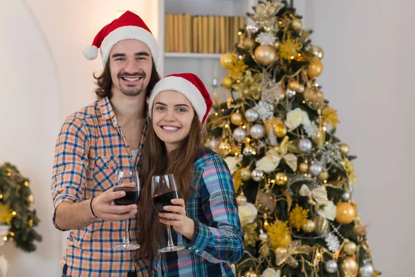 Christmas Holiday Happy Couple Hold Wine Glasses Stand Near Decorated New Year Tree Wear New Year Santa Hat — Stock Photo, Image