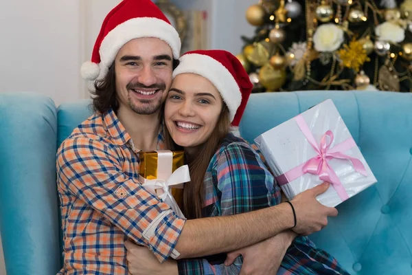 Vánoční dovolená šťastný pár nosit nový rok Santa čepice, muž a žena všeobjímající držení krabičce — Stock fotografie