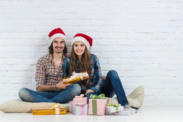 Noel tatil mutlu çift kat giyim yeni yıl Santa şapka kap, erkek ve kadın ile mevcut kutuları gülümseyen oturmak — Stok fotoğraf