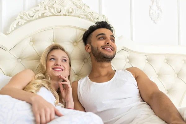 Ungt par liggande i sängen, lyckligt leende spansktalande Man och kvinna som tittar kopiera utrymme — Stockfoto