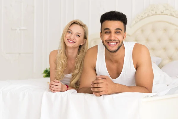 Ungt par liggande i sängen, lyckligt leende spansktalande Man och kvinna — Stockfoto