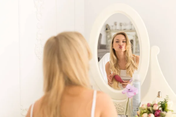 Ξανθιά νεαρή γυναίκα βούρτσα μαλλιών, όμορφο κορίτσι κοιτάζοντας στον καθρέφτη φυσήξει άνεμος φιλιά — Φωτογραφία Αρχείου