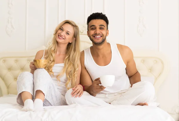 Młoda para pić kawy soku pomarańczowego, siedząc w łóżku, szczęśliwy uśmiech młody hiszpanin mężczyzna i Kobieta — Zdjęcie stockowe