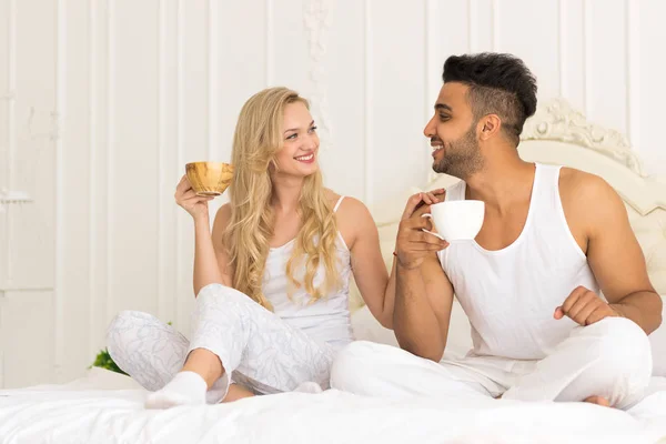 Pareja joven bebe café sentada en la cama, feliz sonrisa joven hispano hombre y mujer —  Fotos de Stock
