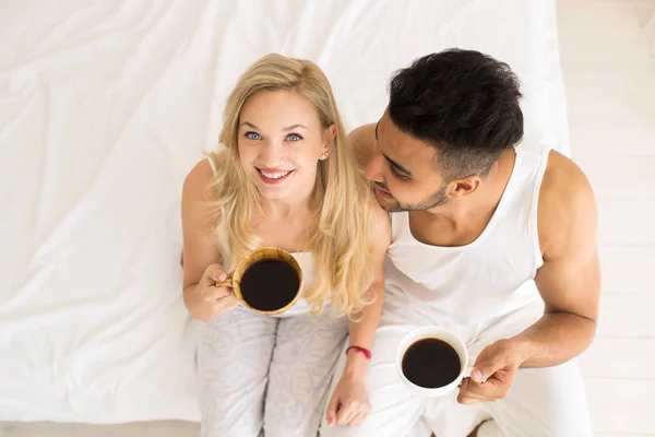 年轻夫妇喝咖啡坐在床上, 快乐的微笑拉美裔男人和女人的顶角视图 — 图库照片