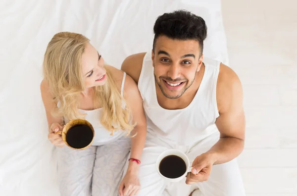 Νεαρό ζευγάρι καφέ ποτό που κάθεται στο κρεβάτι, ευτυχισμένο χαμόγελο Ισπανόφωνος άνδρας και γυναίκα επάνω γωνία θέα — Φωτογραφία Αρχείου