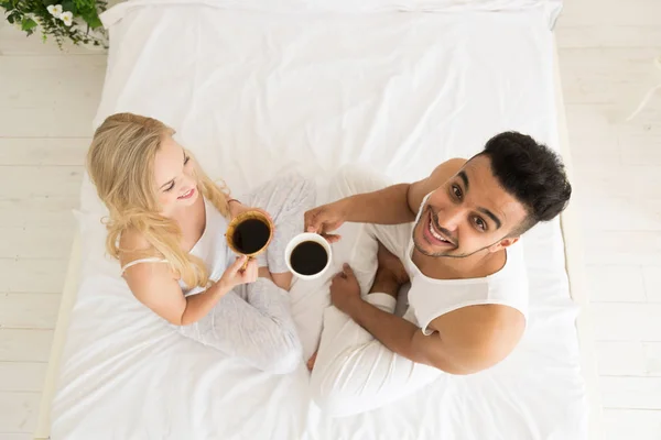 Pareja joven bebe café sentada en la cama, sonrisa feliz Hombre hispano y mujer Vista superior — Foto de Stock