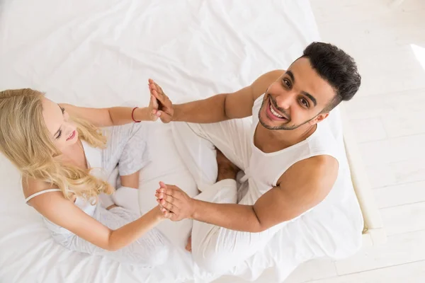 Pareja joven sostiene las manos sentada en la cama, feliz sonrisa Hombre hispano y mujer Top Angle View —  Fotos de Stock