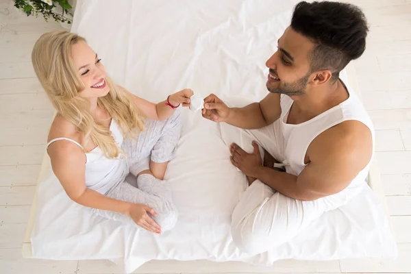 Pareja joven sentada en la cama, mujer sonriente le da protección anticonceptiva a los amantes del condón — Foto de Stock