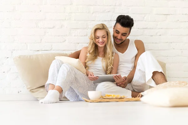 Молода пара сидить на подушках, іспаномовний чоловік і жінка, використовуючи планшет любителів комп'ютерів спальня — стокове фото