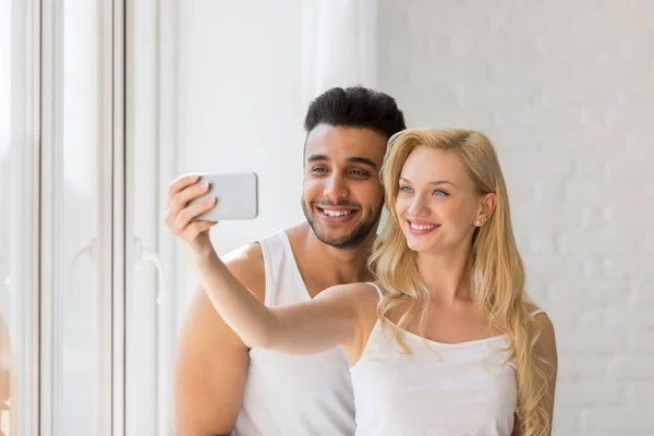 Unga vackra paret utmärker fönster, tar Selfie foto på Smart mobiltelefon — Stockfoto