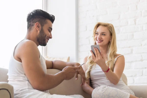 Jonge mooie paar zitten op Coach in de buurt van venster, met behulp van cel slimme telefoon gelukkig glimlach Spaanse Man vrouw — Stockfoto