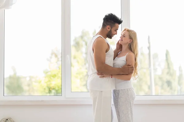 Joven pareja hermosa de pie cerca de la ventana abrazo, feliz sonrisa hispano hombre y mujer —  Fotos de Stock