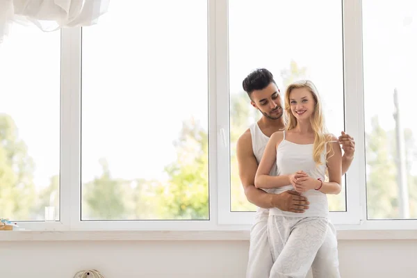 Junges schönes Paar steht in der Nähe von Fenster Umarmung, glückliches Lächeln spanischer Mann und Frau — Stockfoto