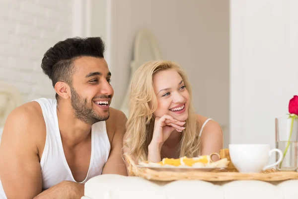 Νεαρό ζευγάρι ξαπλωμένο στο κρεβάτι τρώνε πρωινό πρωί με κόκκινο τριαντάφυλλο λουλούδι, χαρούμενο χαμόγελο Ισπανόφωνος άνδρας και γυναίκα — Φωτογραφία Αρχείου