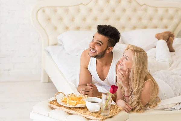 Pareja joven acostada en la cama desayunar por la mañana con flor de rosa roja, feliz sonrisa hispana hombre y mujer —  Fotos de Stock