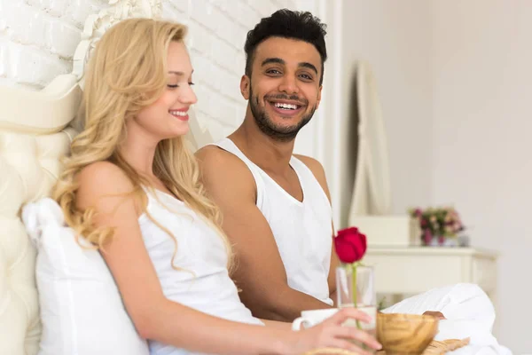 Casal jovem deitado na cama comer manhã com flor de rosa vermelha, sorriso feliz hispânico homem e mulher — Fotografia de Stock