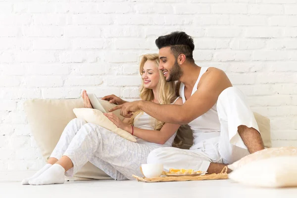 Fiatal pár ül a padló párnák, a Spanyol férfi és a nő segítségével tabletta számítógép szerelmesek hálószoba — Stock Fotó