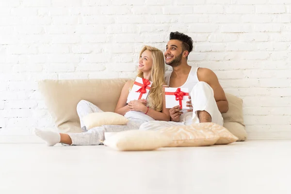 Jeune couple assis sur le plancher d'oreillers, heureux sourire hispanique homme femme tenir l'enveloppe présente avec des amoureux du ruban dans la chambre — Photo