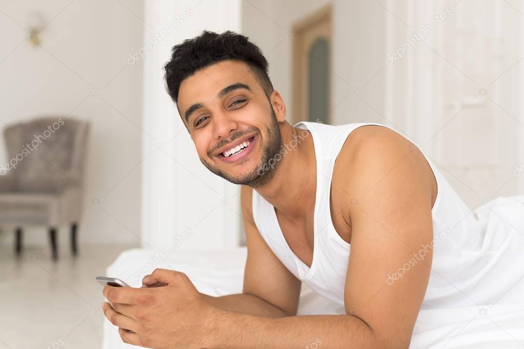 Handsome Hispanic Man Lying In Bed Using Cell Smart Phone, Young Guy Happy Smile