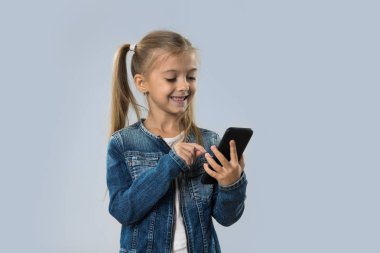 Güzel küçük kız hücre kullanarak akıllı izole telefon mutlu gülümseyerek aşınma Kot ceket