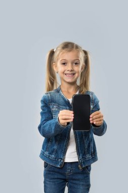 Güzel küçük kız tutun hücre akıllı telefon boş ekran aşınma Kot ceket gülümseyen mutlu izole
