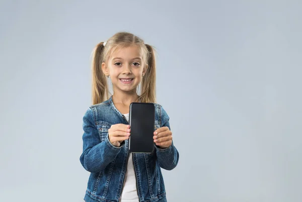 Pequeña adolescente muestra la pantalla del teléfono inteligente celular con espacio vacío de copia, pequeño niño feliz sonriente —  Fotos de Stock