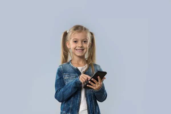 Piękna mała dziewczyna za pomocą komórki Smart Phone szczęśliwy uśmiechający się nosić dżinsy płaszcz na białym tle — Zdjęcie stockowe