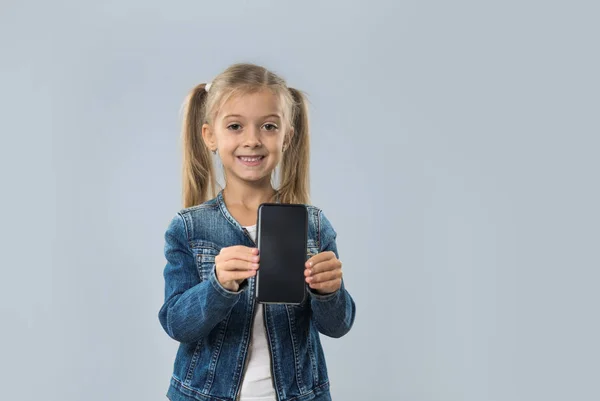 Piękne małe komórki przytrzymaj dziewczyna inteligentny telefon pusty ekran szczęśliwy uśmiechający się nosić dżinsy płaszcz na białym tle — Zdjęcie stockowe