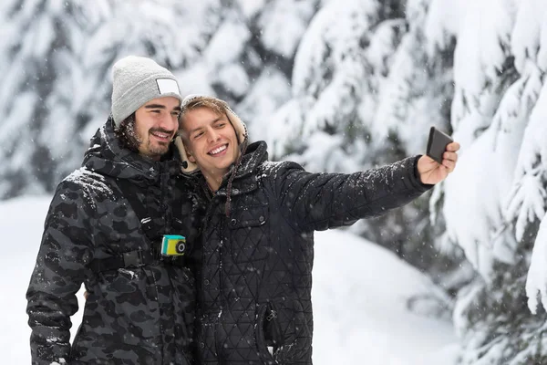 A fiatalember pár vesz Selfie fénykép hó erdőben kültéri srácok tartja kezében — Stock Fotó