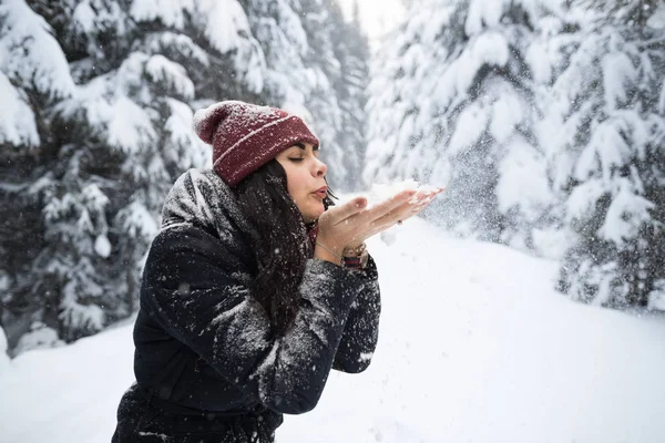 Jovem bela mulher soprar as mãos de neve na floresta de inverno menina ao ar livre andando nevado parque branco Imagem De Stock