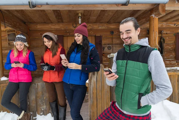 Ομάδα ατόμων χρησιμοποιώντας έξυπνο τηλέφωνο κουβέντα εξωτερική μηνυμάτων Internet ξύλινα χώρα σπίτι χειμώνα χιόνι θέρετρο εξοχικό σπίτι — Φωτογραφία Αρχείου