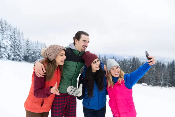 Mulher segura câmera de telefone inteligente tirando selfie foto amigos sorrir neve floresta jovens grupo ao ar livre inverno — Fotografia de Stock