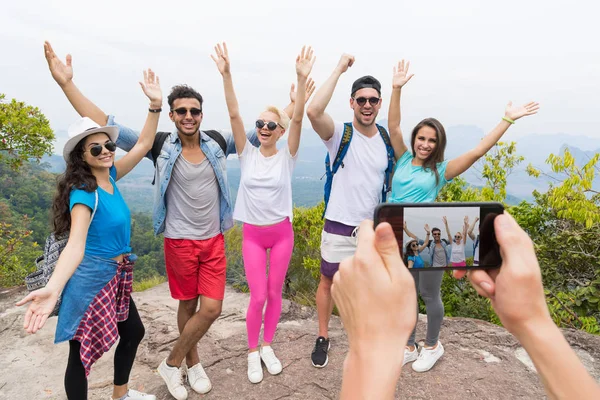 Téléphone intelligent cellulaire prenant la photo du groupe touristique joyeux avec sac à dos sur le paysage du sommet de la montagne, les gens posant — Photo