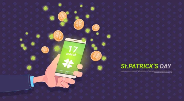 Ręka trzyma inteligentny telefon z liści koniczyny i złote monety na tle Happy St Patricks Day — Wektor stockowy