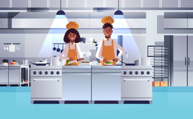 Şefler tahtada taze sebze doğruyor. Üniformalı Afro-Amerikan erkek kadın salata pişirme konsepti hazırlıyor. Modern restoran mutfağı.