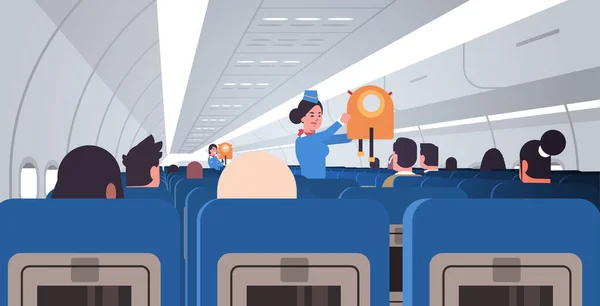 Stewardess stewardess stewardess stewardess uitleggen voor passagiers hoe jas reddingsvest te gebruiken in noodsituatie veiligheid demonstratie concept modern vliegtuig boord interieur horizontaal plat — Stockvector