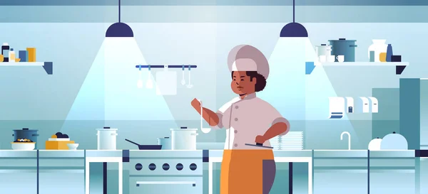 Chef professionista femminile cuoco preparazione e degustazione piatti donna afro-americana in uniforme vicino stufa cottura cibo concetto moderno ristorante cucina interno piatto ritratto orizzontale — Vettoriale Stock