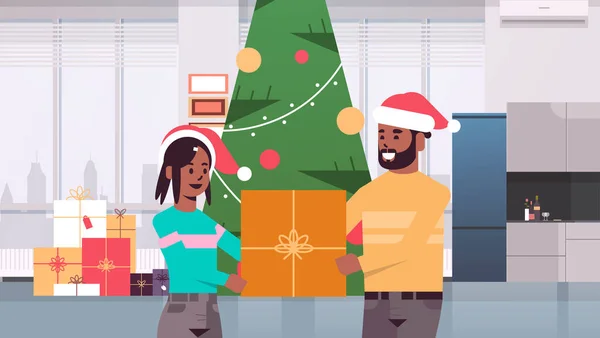 Pareja celebración regalo regalo caja feliz navidad feliz año nuevo celebración concepto hombre mujer vistiendo sombreros de santa de pie cerca del árbol en forma moderna sala de estar interior horizontal retrato — Vector de stock