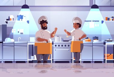 Profesyonel aşçılar yemek hazırlıyor ve tadımlık Afro-Amerikan kadın üniformalı adam soba pişirme konseptinin yanında duruyor modern mutfak iç kısmı düz yatay.