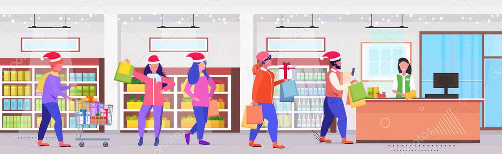people in santa hats with shopping bags standing line queue at cash desk with female cashier christmas holidays celebration concept modern retail store interior full length horizontal