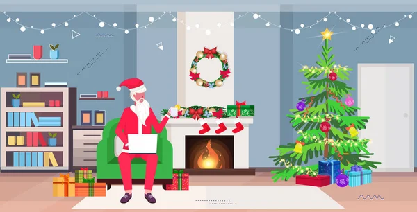 Santa Claus sedí v křesle pomocí notebooku a pití čaje moderní obývací pokoj s krbem jedle a dárkové krabice veselé Vánoce Nový rok svátky koncepce oslavy horizontální plné délky — Stockový vektor