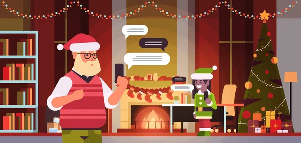 Santa con elfo femmina helper chatta utilizzando l'app mobile su smartphone social network chat bolla concetto di comunicazione moderno salotto interno ritratto orizzontale — Vettoriale Stock
