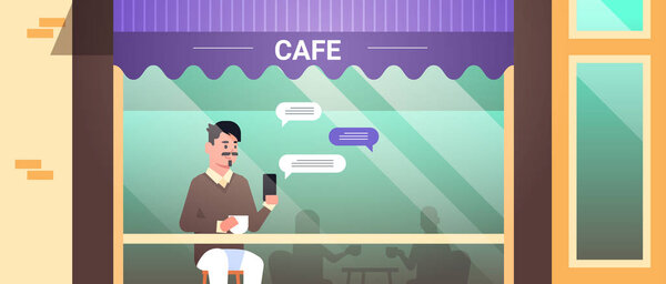 посетитель сидит за столом с помощью чата мобильного приложения на смартфоне социальная сеть чат пузырь концепции коммуникации уличное кафе внешний портрет горизонтальный
