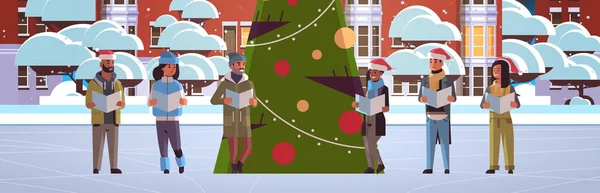 Mix ras mensen lezen boeken vrolijk kerstmis gelukkig nieuwjaar vakantie viering concept mannen vrouwen dragen santa hoeden staan in de buurt fit boom modern stadsgezicht achtergrond horizontaal volledige lengte — Stockvector