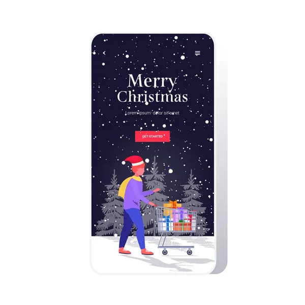 Hombre en Santa Claus sombrero empujando carro carro con regalo regalo regalo cajas feliz navidad feliz año nuevo vacaciones celebración concepto smartphone pantalla aplicación móvil en línea longitud completa boceto — Vector de stock