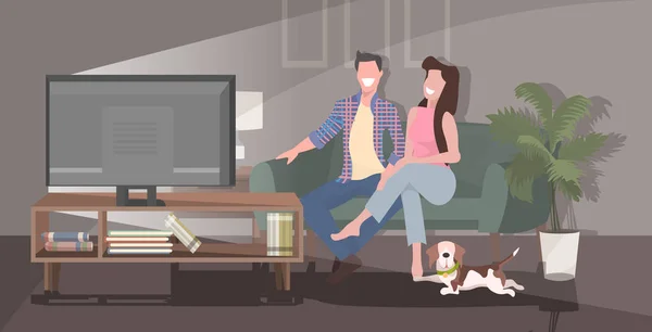 Pasangan bahagia menonton tv tersenyum pria wanita duduk di sofa di rumah menghabiskan waktu bersama-sama ruang tamu modern interior penuh horisontal - Stok Vektor